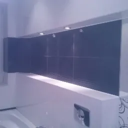 Wykończona łazienka z szarymi płytkami strukturalnymi, oświetleniem punktowym i dekoracyjnymi motywami kwiatowymi na białych płytkach. Lustro odbija fragment łazienki.