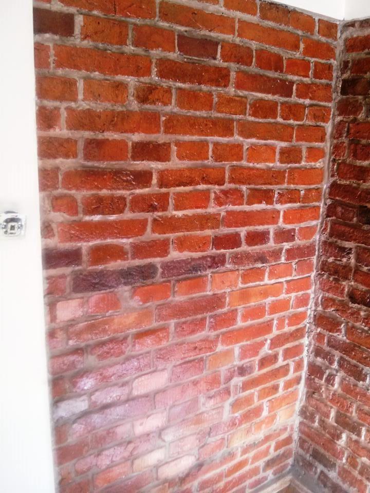 Ściana wykończona tapetą imitującą czerwoną cegłę, widoczny fragment białej ściany i narożnik. Realistyczne odwzorowanie faktury cegły.