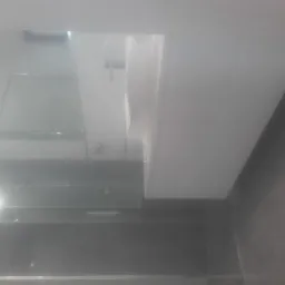 Nowoczesna łazienka z czarnymi płytkami i białą armaturą widziana pod kątem, z widoczną szklaną kabiną prysznicową i oświetleniem.