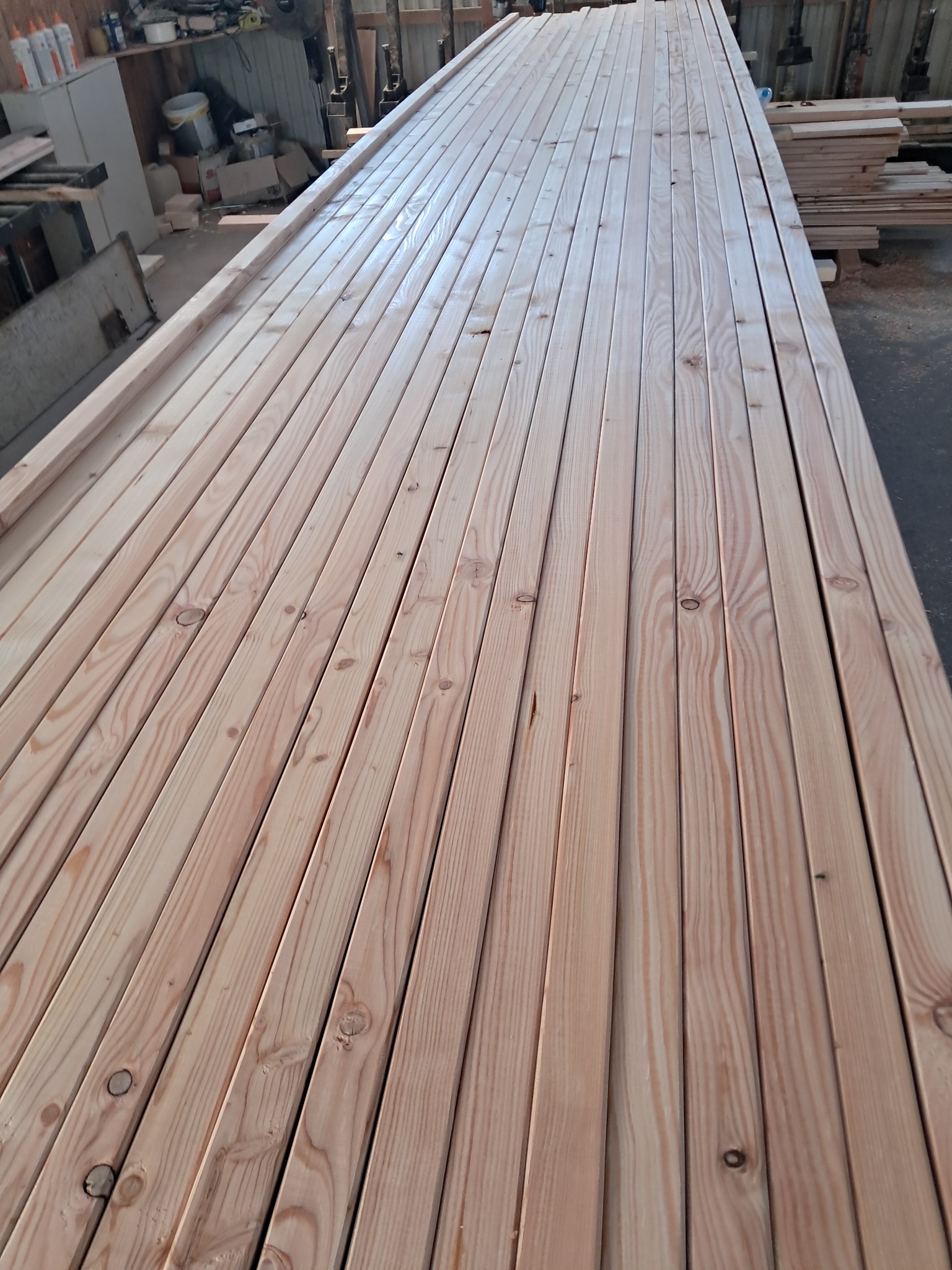 Równy stos jasnych, świeżo obrobionych desek z widocznymi słojami drewna, ułożonych jedna obok drugiej, gotowych do dalszej obróbki lub transportu.