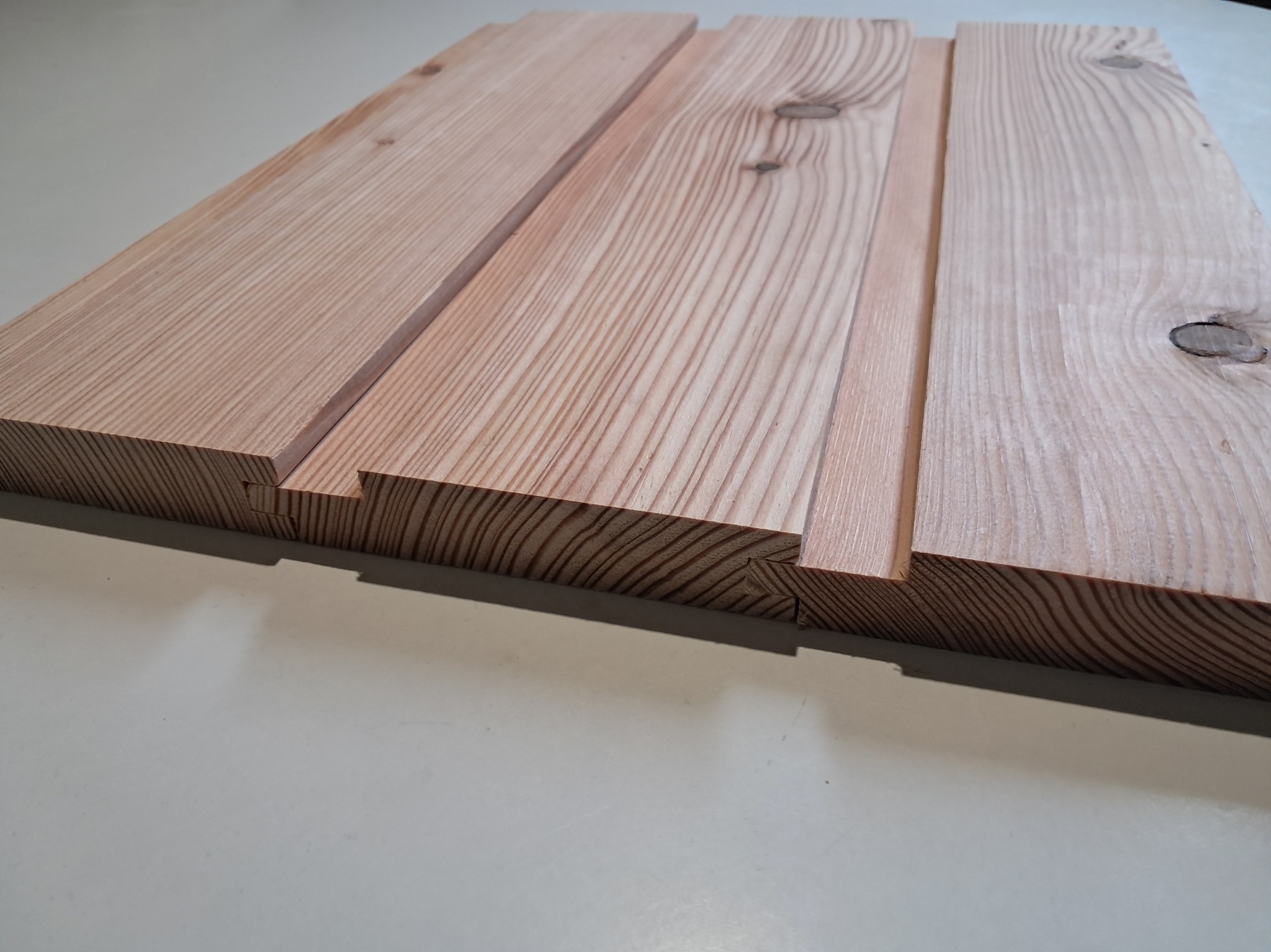 Fragment obrobionej deski z widocznymi słojami drewna i połączeniem na pióro i wpust, ukazujący precyzję wykonania.