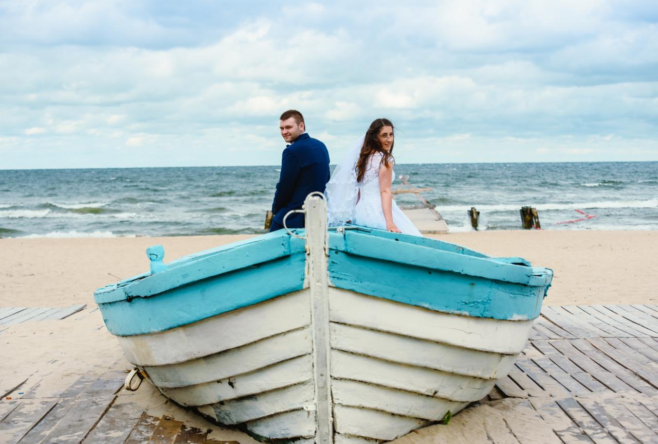 Para młoda siedząca w łodzi na plaży, widok na morze i pochmurne niebo w tle.