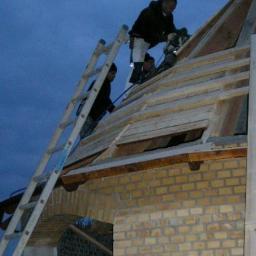 Cmj Design Totalentreprise - Ekipa budowlana pracuje na dachu rozbudowywanego domu z żółtej cegły, widoczna drabina i narzędzia.