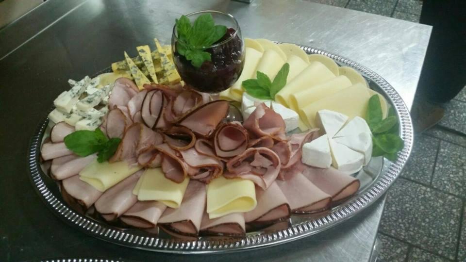 Srebrna taca z różnorodnymi serami, wędlinami i konfiturą w kieliszku, udekorowana listkami mięty, na metalowym blacie.