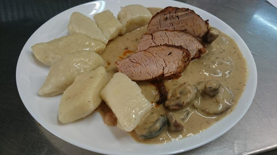 Porcja obiadowa na białym talerzu: kluski ziemniaczane, plastry pieczeni wieprzowej w sosie grzybowym, ujęcie z bliska.