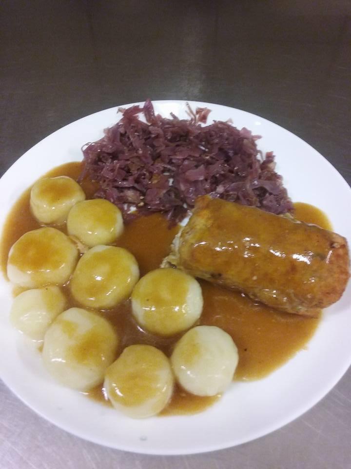 Porcja obiadowa na białym talerzu: roladka mięsna w sosie, knedle ziemniaczane polane sosem i duszona czerwona kapusta.
