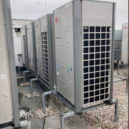 KLIMAT PAWEŁ ŚWIDERSKI - Rząd zewnętrznych jednostek klimatyzacyjnych LG Multi V 5 na dachu budynku komercyjnego, zamontowanych na metalowej konstrukcji z rozsypanymi kamieniami.