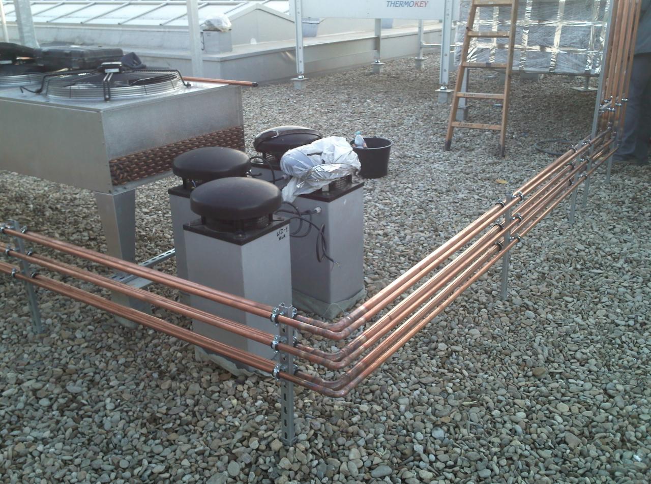 Instalacja chłodnicza na dachu pokrytym żwirem, widoczne miedziane rury, wentylatory, drabina i fragment urządzenia THERMOKEY.