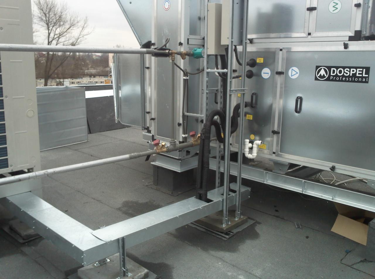 Instalacja przemysłowej wentylacji marki Dospel na płaskim dachu, z widocznymi rurami, zaworami i elementami mocującymi.