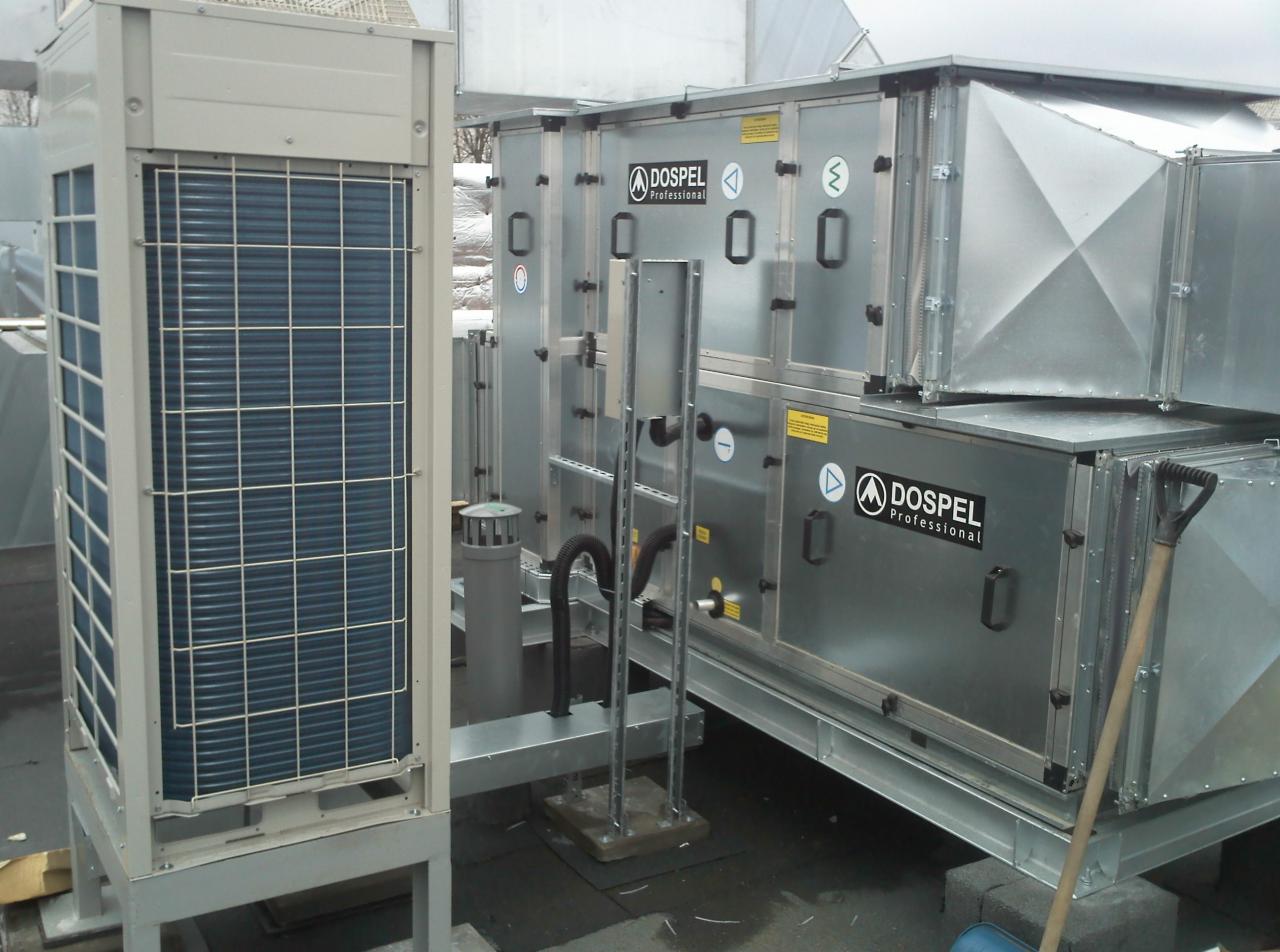 Zewnętrzna instalacja wentylacyjna Dospel Professional na dachu budynku, widoczna jednostka z kratką ochronną i modułowa centrala wentylacyjna z czarnymi uchwytami, szara rura wentylacyjna...