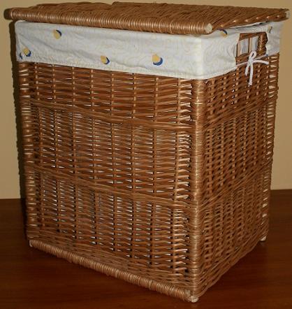 Wiklinowy kosz z pokrywą, wykończony tkaniną w delikatny wzór, na drewnianej podłodze. Widoczna faktura plecionki i detale wykończenia.