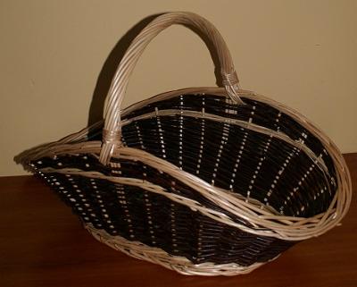 Czarno-beżowy, pleciony kosz z uchwytem, ustawiony na drewnianym blacie, na tle ściany w ciepłym odcieniu beżu. Widoczna faktura plecionki i detale wykonania.