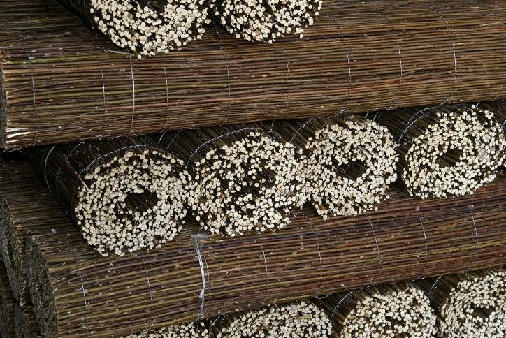 Stos brązowych, ciasno zwiniętych mat trzcinowych, związanych drutem, z widocznymi jasnymi końcówkami trzcin, ułożonych jeden na drugim.