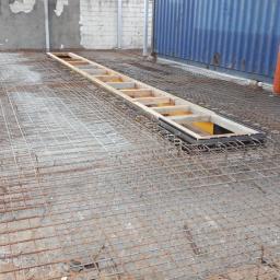 DOM-BET-BUD Wojciech Cichulski - Przygotowanie zbrojenia pod wylewkę, widoczna siatka zbrojeniowa na gruncie, szalunek pod kanał rewizyjny oraz fragment kontenera w tle.