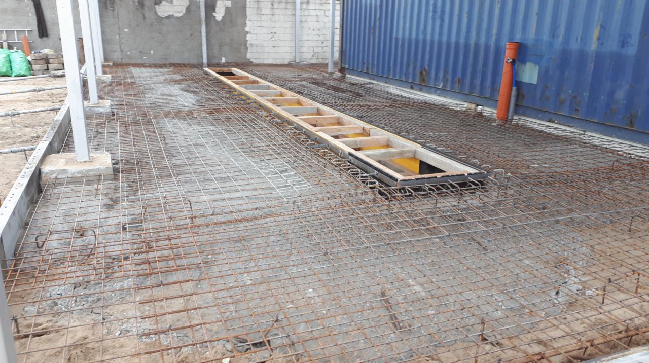 Przygotowanie zbrojenia pod wylewkę, widoczna siatka zbrojeniowa na gruncie, szalunek pod kanał rewizyjny oraz fragment kontenera w tle.