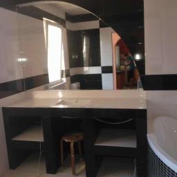 JAROSZY - Wykończona łazienka z biało-czarnymi płytkami, dużym lustrem i zabudowaną umywalką z półkami, widoczna osoba w tle.