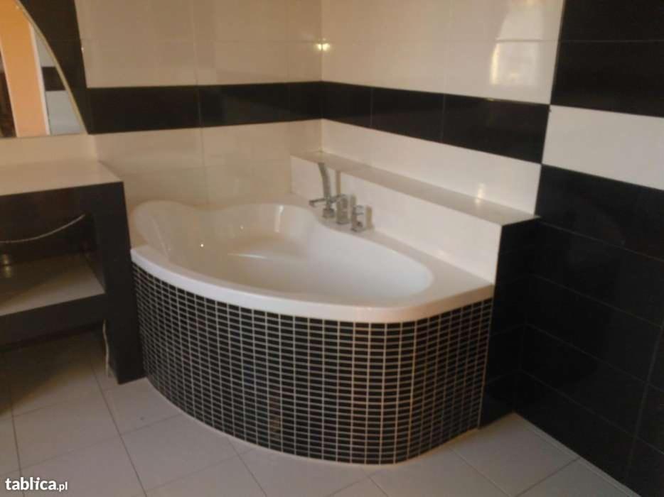 Biała wanna narożna obudowana czarną mozaiką w łazience z biało-czarnymi płytkami ułożonymi w poziome pasy.