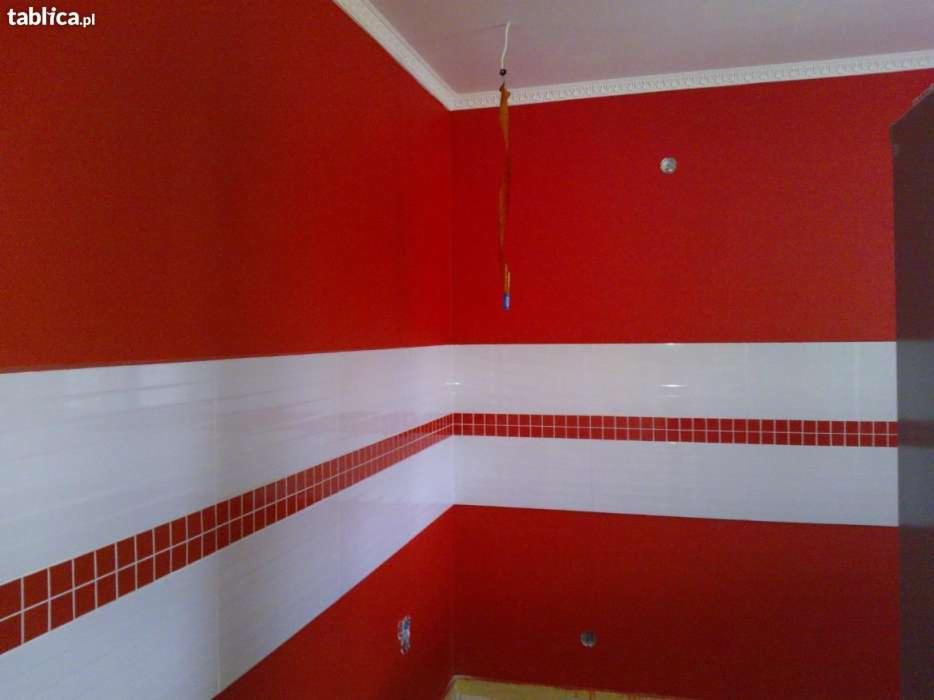 Intensywnie czerwone ściany w pomieszczeniu z białymi płytkami i bordową mozaiką, widoczne przewody elektryczne na suficie.