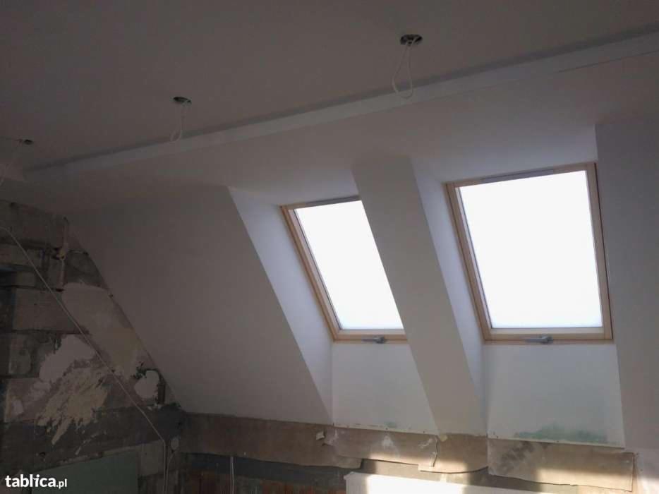 Poddasze w trakcie prac wykończeniowych: dwa okna dachowe w drewnianych ramach, gładzie na skośnych ścianach, widoczne niedoskonałości i przygotowania do malowania, wystające kable oświetleniowe.
