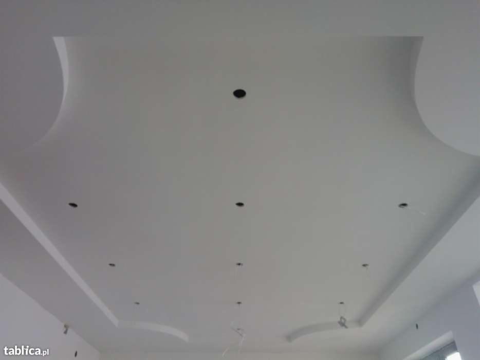 Biały, podwieszany sufit z dekoracyjnymi elementami gipsowymi i otworami na oświetlenie punktowe, widok z dołu.