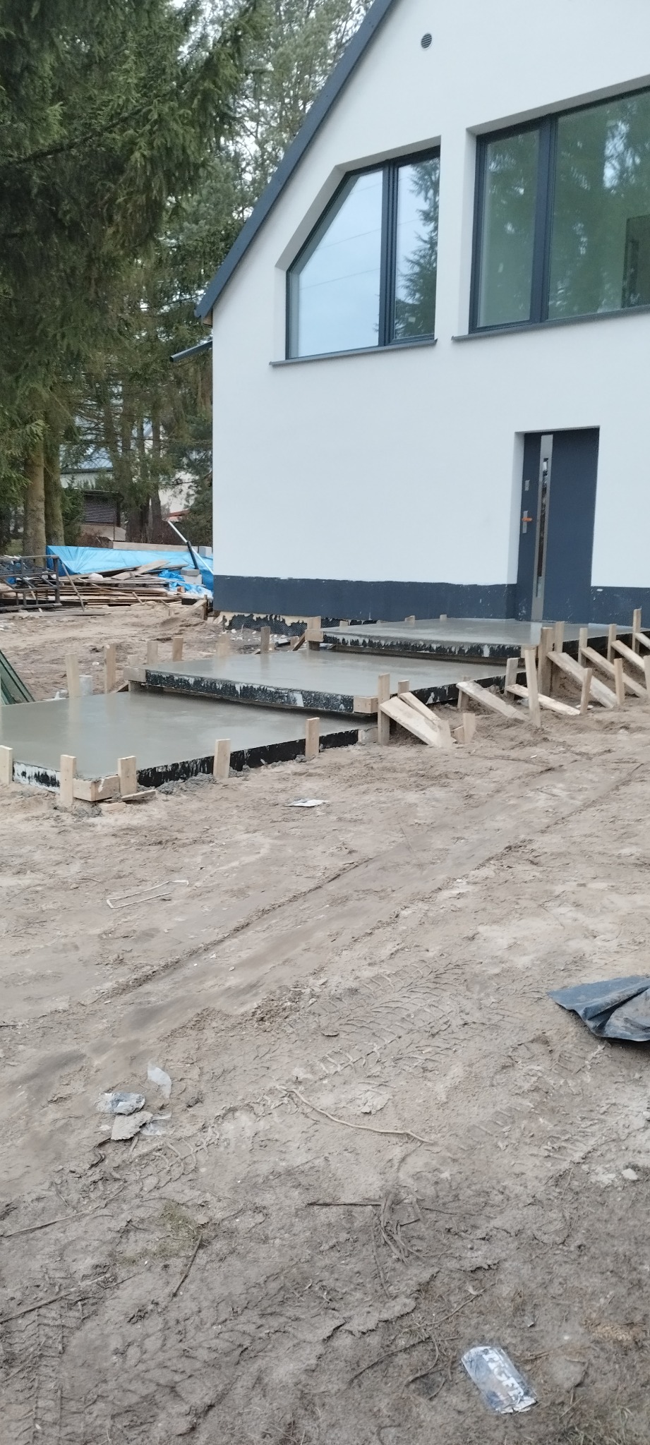 Wylewka betonowa przed nowoczesnym domem jednorodzinnym, widoczne szalunki i świeży beton, teren wokół domu częściowo przygotowany.