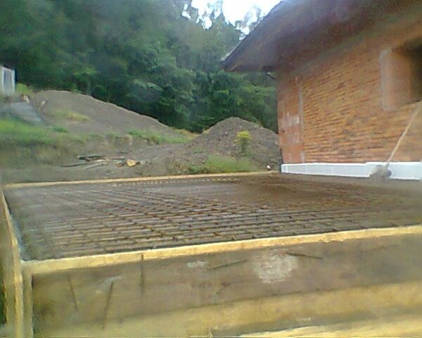 Zbrojenie fundamentów pod budynek z czerwonej cegły, widok z góry na siatkę zbrojeniową w drewnianej szalunku, w tle zielone wzgórze i drzewa.