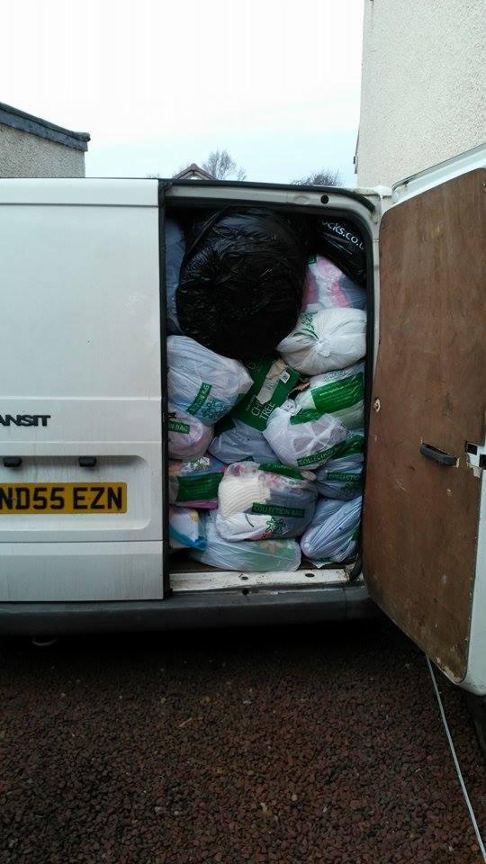 Biały van Ford Transit załadowany workami z odzieżą używaną, widoczne tablice rejestracyjne ND55 EZN, otwarte tylne drzwi.