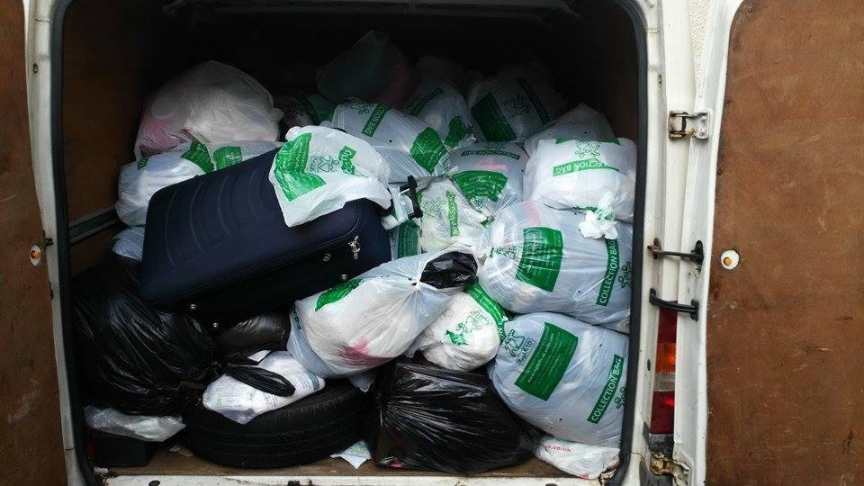Wnętrze furgonetki wypełnionej workami z odzieżą używaną i walizką, gotowej do transportu. Widoczne worki z napisem 'Collection Bag' i ciemna walizka.
