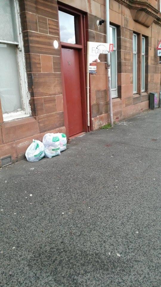 Trzy worki z odzieżą używaną leżą przed budynkiem z czerwonymi drzwiami, obok szyldu 'Future'.