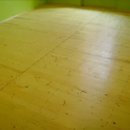 Jasna, drewniana podłoga z widocznymi słojami, świeżo po renowacji. Zielona ściana w tle. Widok z góry, oświetlenie naturalne.