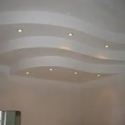 Biały sufit z dekoracyjnymi, falistymi wgłębieniami i punktowym oświetleniem LED. Widoczne fragment okna w lewym dolnym rogu.