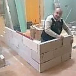 Murarz w trakcie wznoszenia ścianki działowej z białych bloczków, widoczny na tle surowego wnętrza w trakcie prac wykończeniowych.