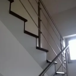 Nowoczesne schody z balustradą ze stali nierdzewnej, widok z dołu, podkreślający minimalistyczny design i precyzję wykonania. Widoczne elementy mocowania.