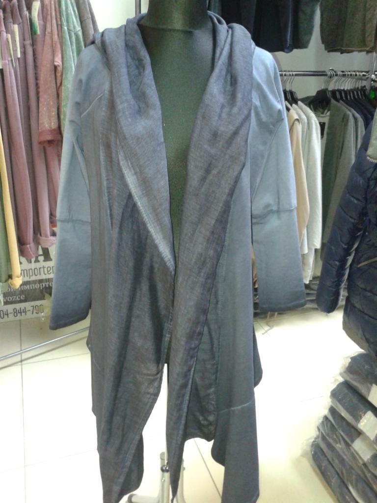 Asymetryczny, szaro-niebieski kardigan z kapturem na manekinie, z wyraźną fakturą materiału i drapowaniem. W tle wieszaki z ubraniami w sklepie.