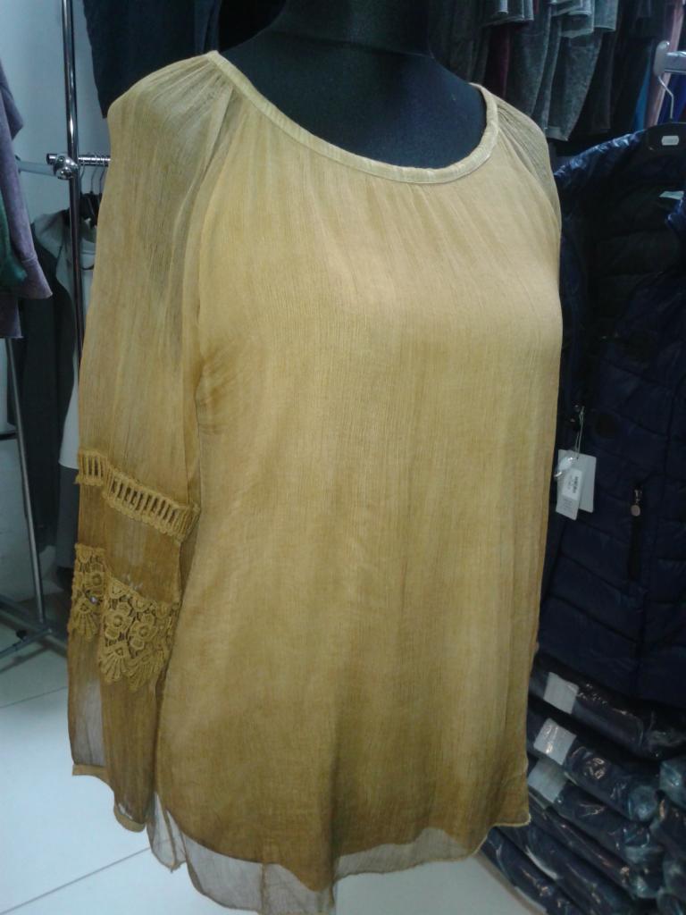 Delikatna, złota bluzka z koronkowymi wstawkami na rękawach, zaprezentowana na manekinie na tle sklepowego asortymentu. Subtelna faktura materiału.