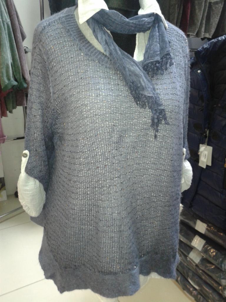 Szaro-błękitna, ażurowa tunika z długim rękawem i szalem z koronką, zaprezentowana na manekinie. Widoczne białe mankiety i sterta ubrań w tle.