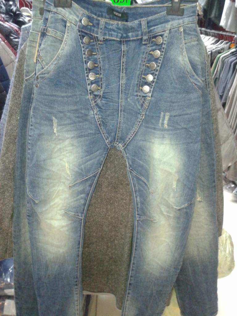 Niebieskie jeansy damskie z wysokim stanem i rzędem guzików, wiszące na wieszaku w sklepie odzieżowym w Rzgowie. Widoczne przetarcia i detale szwów.