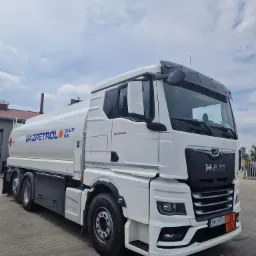 Cysterna MAN Gazpetrol z oznaczeniami UN 1202 na parkingu, widok z przodu i boku, błękitne niebo w tle.