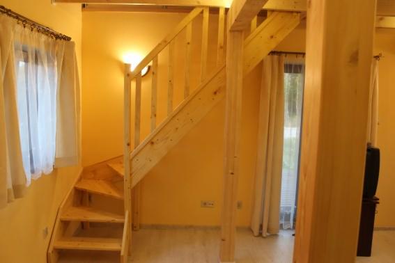 Drewniane schody spiralne w jasnym wnętrzu domu, widok z dołu, naturalne oświetlenie, żółte ściany i zasłony w tle. Elementy konstrukcyjne z surowego drewna.