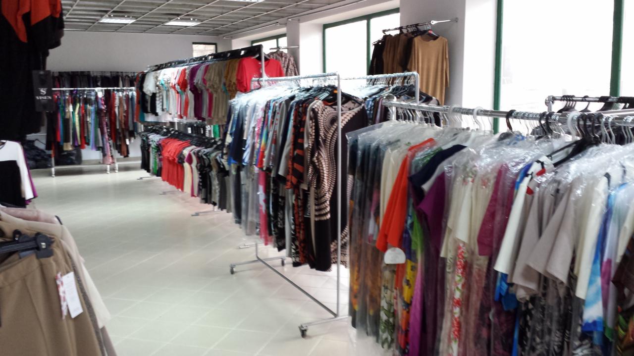 Wnętrze sklepu odzieżowego z rzędami ubrań damskich na wieszakach, oświetlonych światłem dziennym wpadającym przez okna.