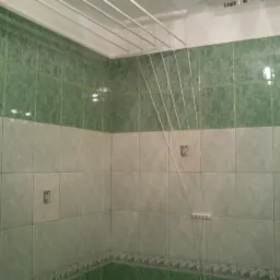 Wykończona łazienka z zielono-białymi płytkami i podwieszaną suszarką na pranie. Widoczne detale płytek i suszarki.