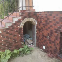 Wykończenie elewacji cegłą klinkierową w Kruszwicy, widoczne schody i łukowe wejście do piwnicy w trakcie prac. Detale mocowania płytek.