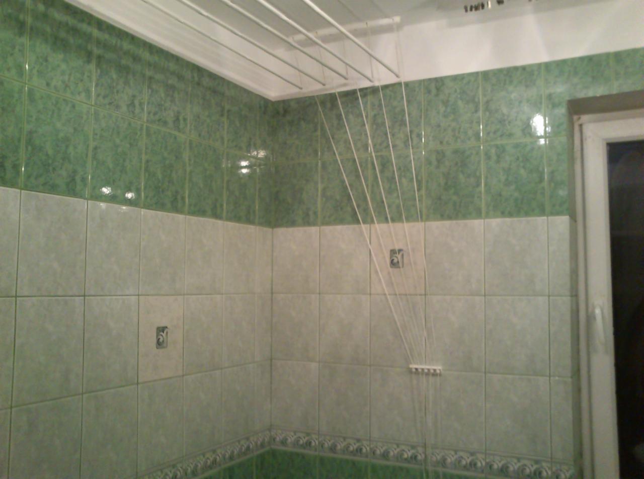 Wykończona łazienka z zielono-białymi płytkami i podwieszaną suszarką na pranie. Widoczne detale płytek i suszarki.