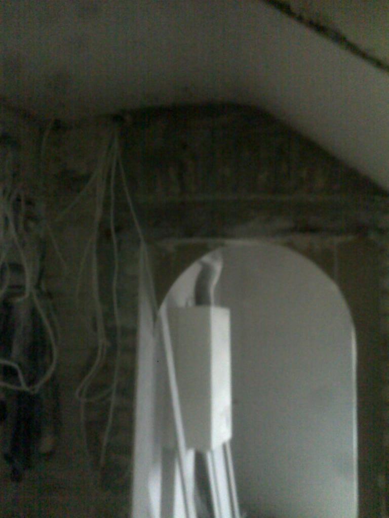 Wnętrze w trakcie remontu z widocznymi przewodami elektrycznymi zwisającymi z sufitu i przygotowanym łukowym otworem w ścianie.