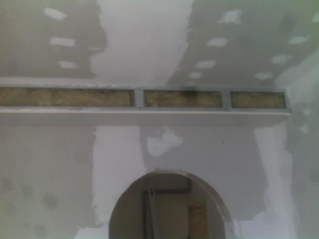 Przygotowanie do montażu podwieszanego sufitu: widoczne profile i ocieplenie we wnęce, ściany w trakcie szpachlowania, łuk wejścia do innego pomieszczenia.