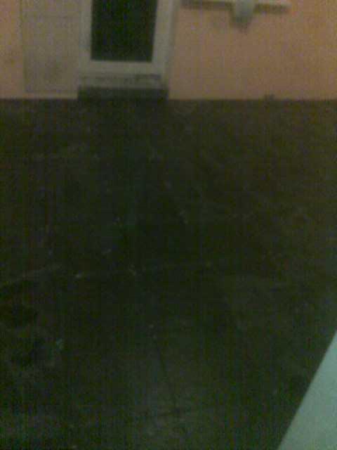 Ciemna, świeżo wylana posadzka betonowa w pomieszczeniu z drzwiami, widoczne ślady po narzędziach.