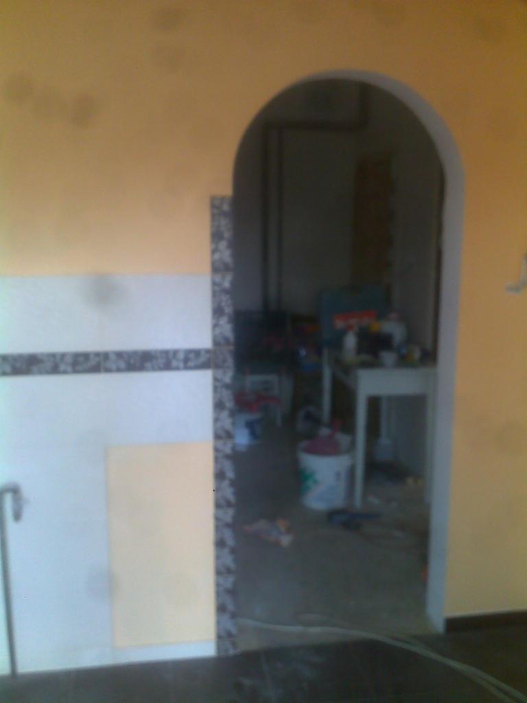 Przygotowania do prac wykończeniowych w Szczecinie: widok na przejście łukowe z widocznymi śladami wcześniejszych prac, częściowo wykończona ściana z płytkami i przygotowana powierzchnia...