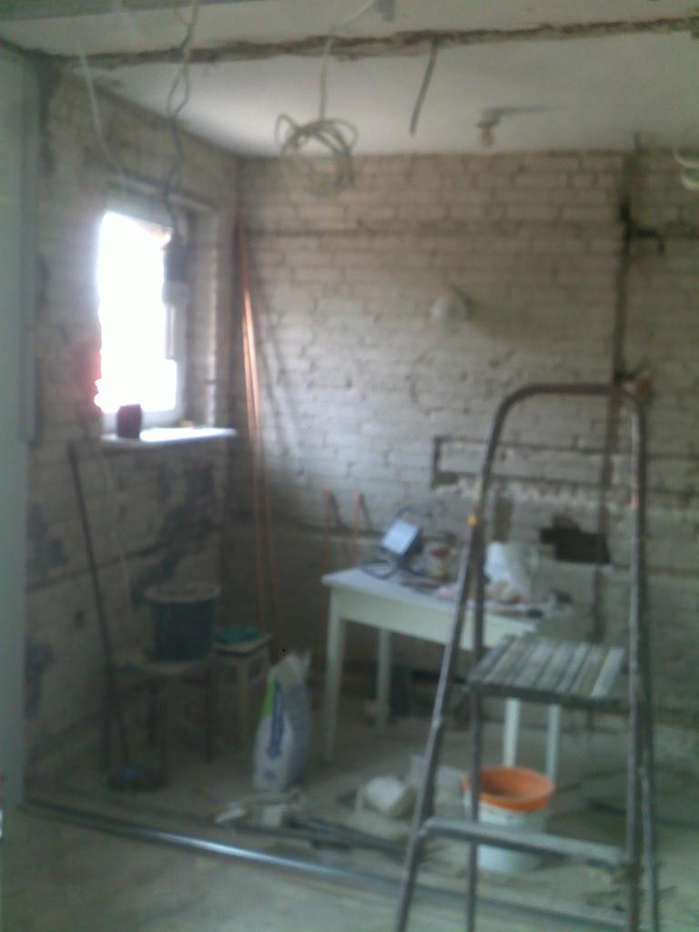 Wnętrze w trakcie remontu: surowe cegły, wiszące kable, drabina, stół z narzędziami, widoczne ślady po skuciu tynku.