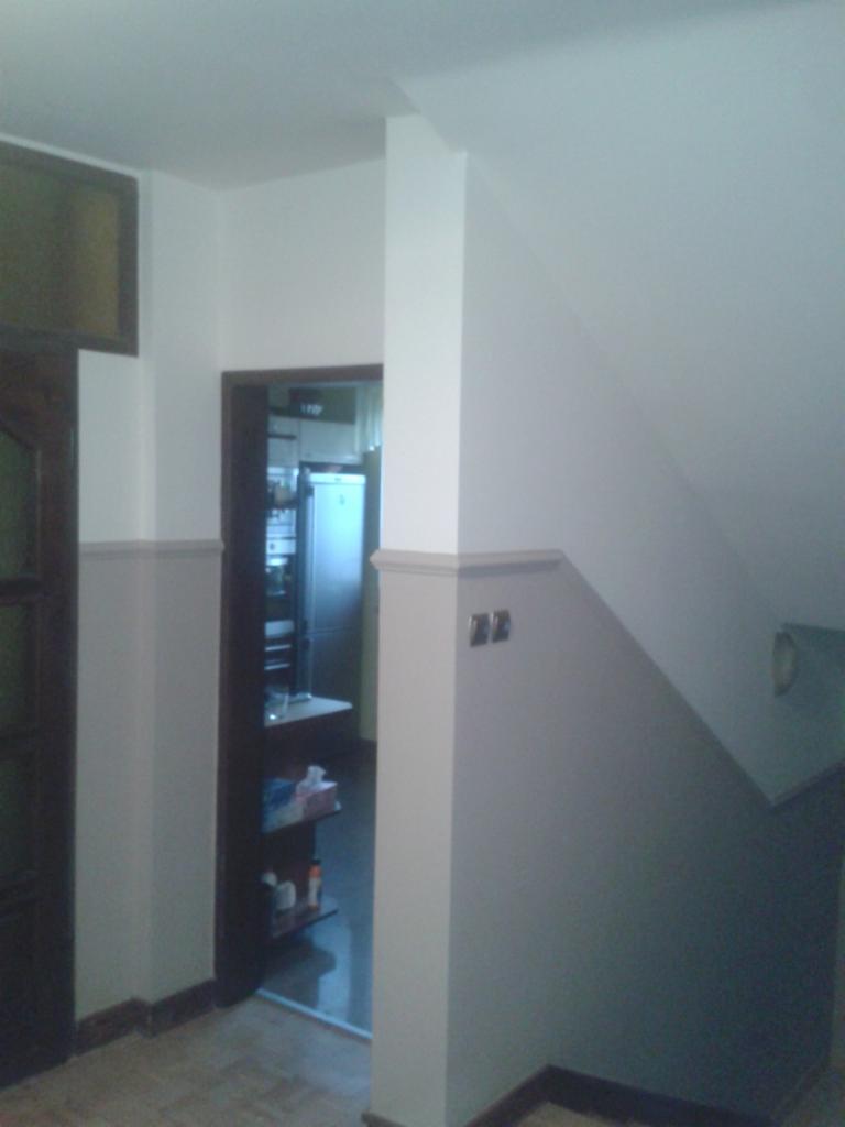 Świeżo pomalowane wnętrze z widocznym fragmentem korytarza i kuchni, akcentującym dwukolorowe ściany i czyste wykończenie, z ciemną ościeżnicą drzwiową.