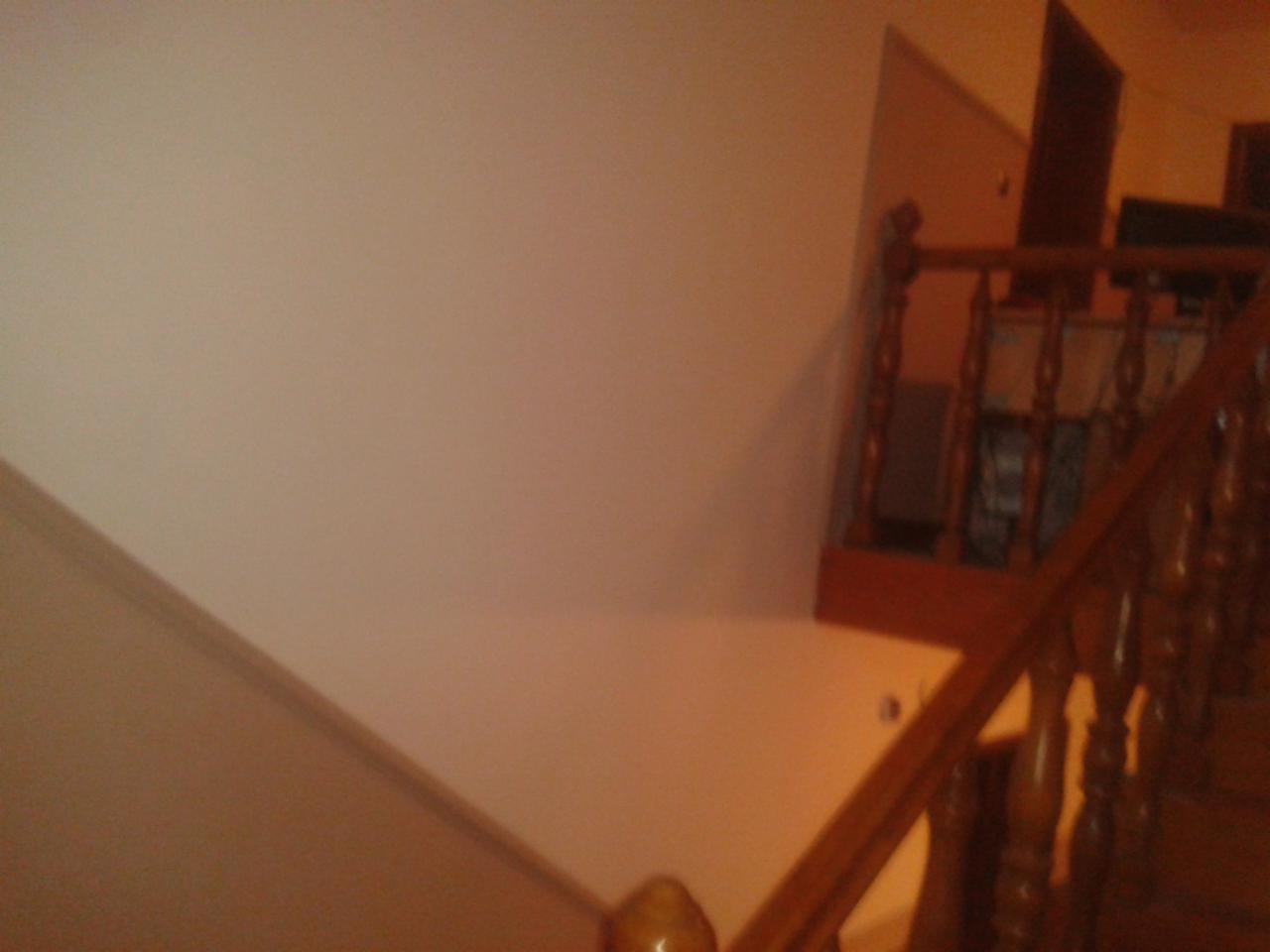 Gładka, kremowa ściana po szpachlowaniu, widoczna z góry, z drewnianą balustradą schodów. Wykończenie wnętrz w domu w Studzionce.